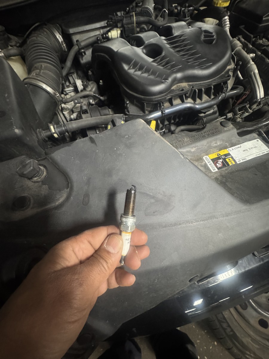 Spark plug inspection beside a vehicle engine bay